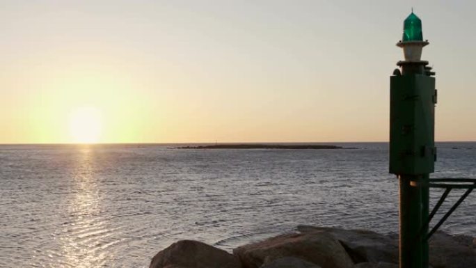 日出或日落时的海洋全景镜头，前景是港口中的一座小灯塔