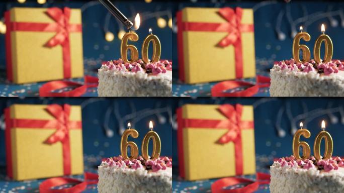 白色生日蛋糕60号点火器燃烧的金色蜡烛，蓝色背景带灯和用红丝带捆绑的礼物黄色盒子。特写