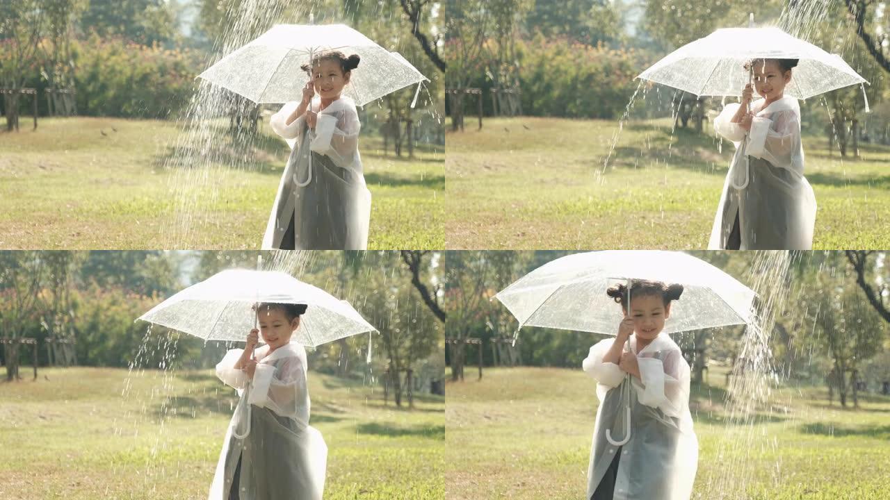 小女孩穿着雨衣和透明伞在花园里玩人造雨晨光