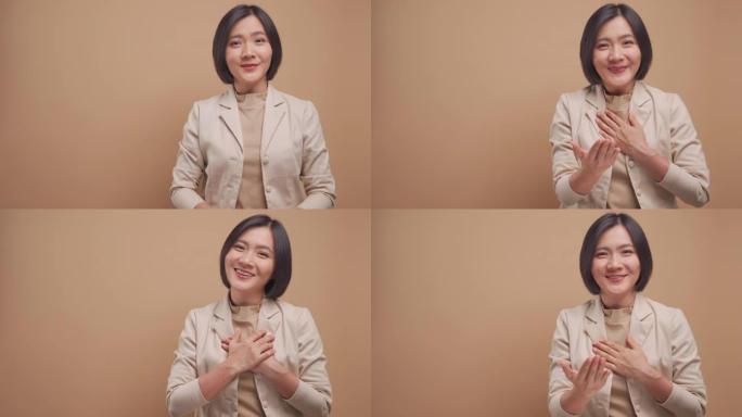 亚洲女商人看着相机开心地微笑着，用手语说谢谢，复制空间隔离在米色背景上。4k视频