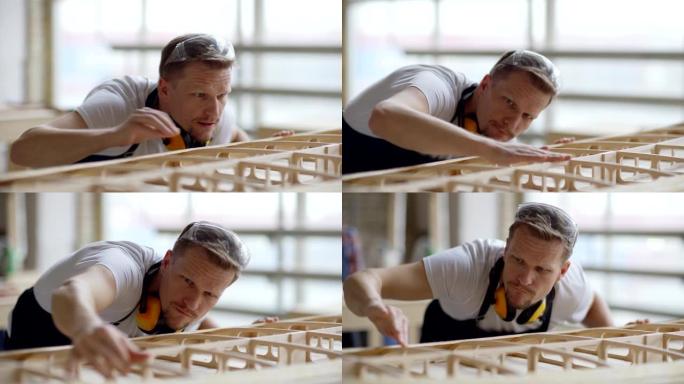 细心的中年木匠的特写镜头，检查放置在木工车间工作台上的未完成的木船模型