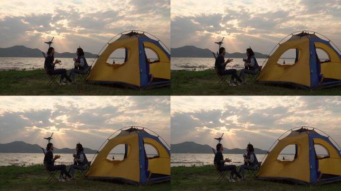 两个十几岁的亚洲女孩唱歌和弹吉他快乐享受日落时湖边的旅行露营。露营概念