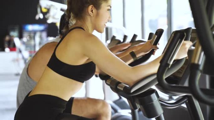 迷人的亚洲女性在健身房骑着健身自行车，看着相机。健康和减肥的生活方式