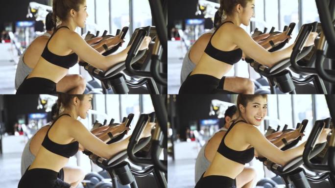 迷人的亚洲女性在健身房骑着健身自行车，看着相机。健康和减肥的生活方式