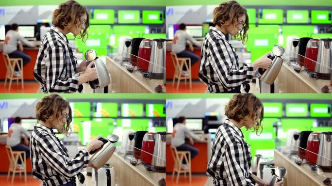 侧面的一个年轻愉快的积极吸引女人在格子衬衫选择电子水壶在家用电器商店，站在一排，拿着和检查银水壶