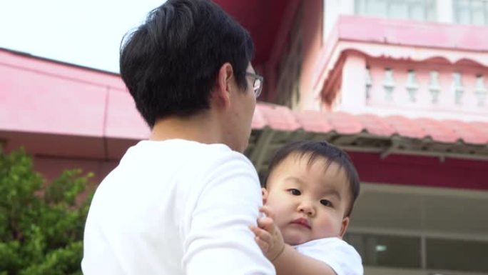 慈爱的父亲举起快乐的亚洲婴儿，站在他们家门前与孩子玩耍