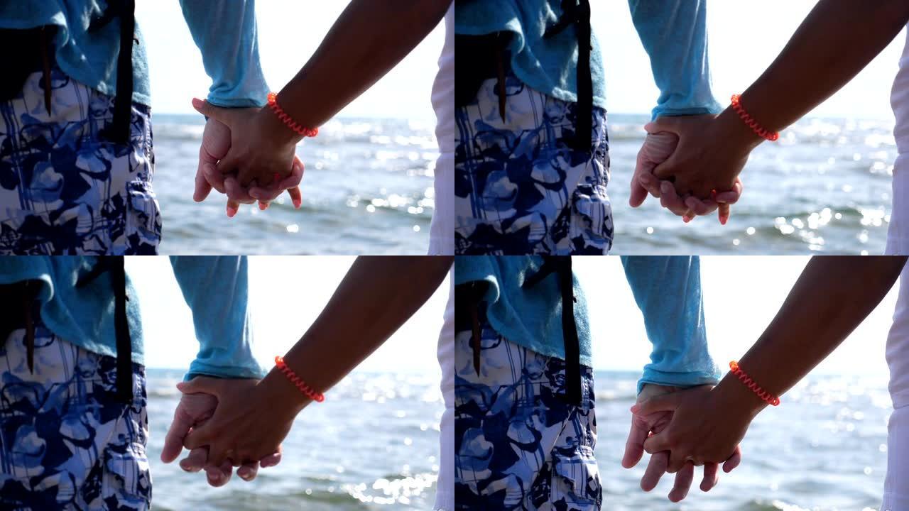 一对年轻的恋人手牵手，站在海边互相调情。几个旅行者在度假期间一起度过时光。背景下美丽阳光明媚的海景。