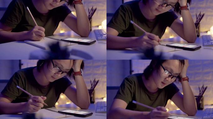 亚洲女人在笔记本上写字，晚上使用智能手机。移动相机视差效果。