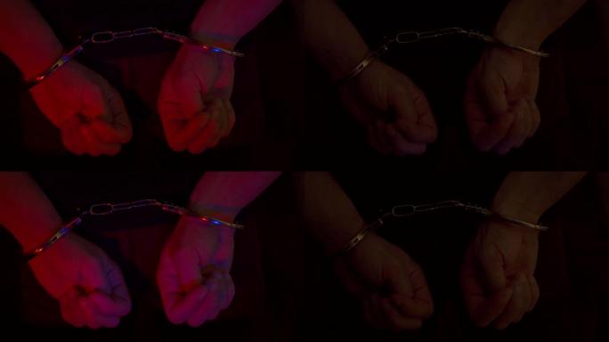 被捕男子戴着手铐。戴着手铐的手被警察的闪光器照亮。闪烁着蓝色和红色。