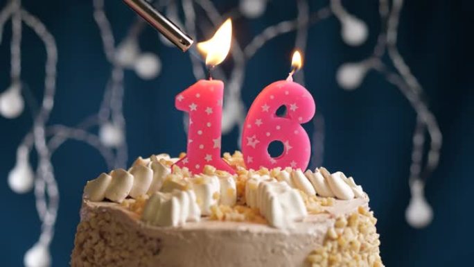 蓝色背景上有16号粉色蜡烛的生日蛋糕。蜡烛着火了。慢动作和特写视图