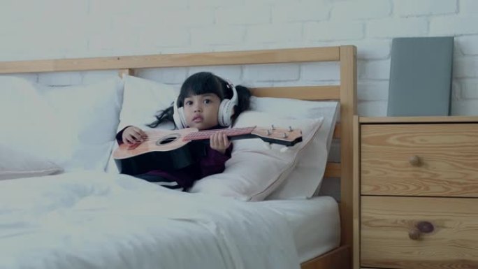 亚洲女孩在床上玩四弦琴，在家快乐的爱好