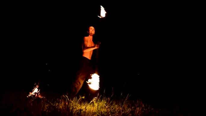 低调。长发，裸露躯干的年轻男性在黑色夜晚视频慢动作中在户外旋转燃烧的火炬。现代法克尔 (fakir)