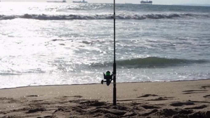 钓鱼竿和渔线轮站在沙滩上的沙滩上，在黄昏时捕捉海鱼