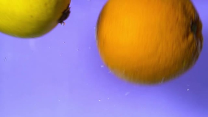 橙色和柠檬在慢动作的紫色背景下滴落并在水中旋转