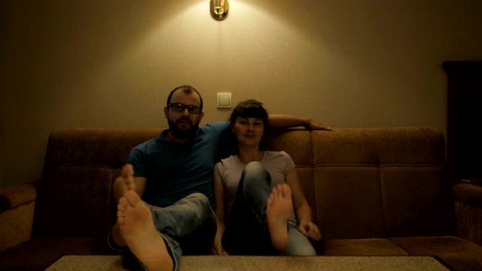 夫妻在电视上看电影。放松的夫妇在舒适的客厅的沙发上看电视。一对恋人在客厅的沙发上看电视。