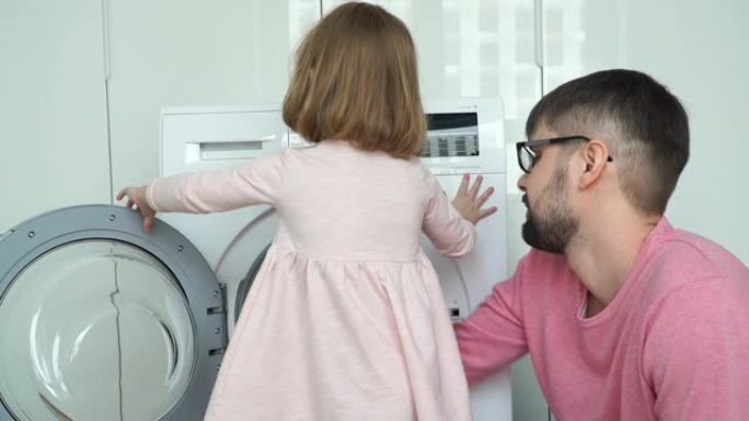 肖像快乐的小微笑3岁的女儿与父亲把柔软的玩具清洗，关闭舱门和打开家用电器。家庭概念