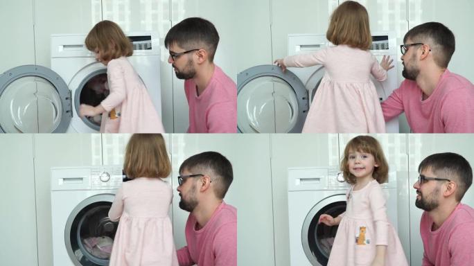 肖像快乐的小微笑3岁的女儿与父亲把柔软的玩具清洗，关闭舱门和打开家用电器。家庭概念