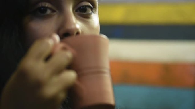 一个微笑的年轻休闲黑发中东女孩的肖像拿着陶器咖啡茶杯，在家自然光线下喝早茶
