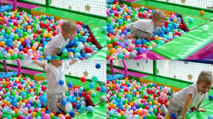 金发小男孩在不同的侧面散球，躺在游戏中心大干划水池中的多色塑料球上。对着镜头微笑。在游戏室玩得开心。