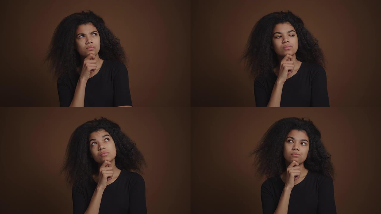 沉思的非洲裔美国女孩在孤立的棕色墙壁背景上思考