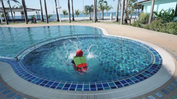 快乐的亚洲儿童男孩穿着救生衣和游泳衣穿着游泳镜跳进泳池度假村。节日快乐。慢动作