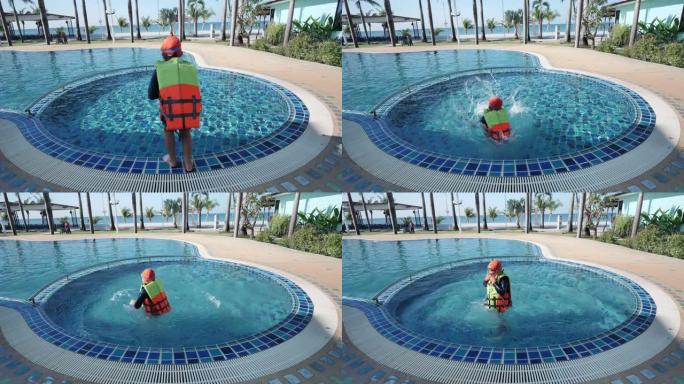 快乐的亚洲儿童男孩穿着救生衣和游泳衣穿着游泳镜跳进泳池度假村。节日快乐。慢动作