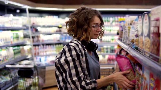 一位戴着耳机的年轻女子的侧视图在杂货店选择燕麦片和薄片，这是早餐的完美食物。阅读标签，选择最好的薄片