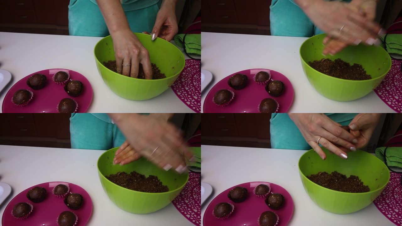 女人用手滚动饼干团。团块是棕色的，由饼干和可可屑制成，并添加黄油。旁边是一盘蛋糕空白。做一个土豆蛋糕