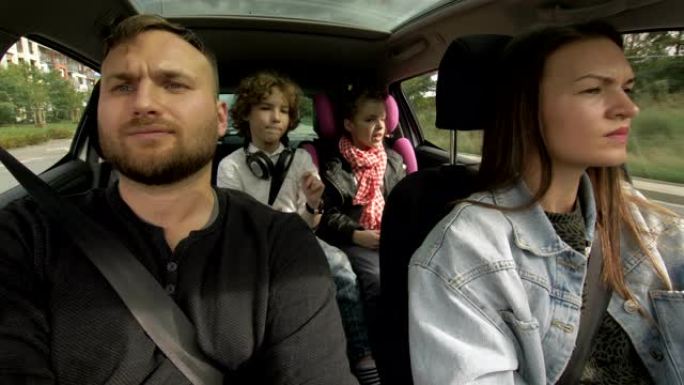 从行驶中的车内拍摄: 女人像快乐的男人一样开车，坐在乘客座位上，与坐在后面的小女孩和男孩聊天