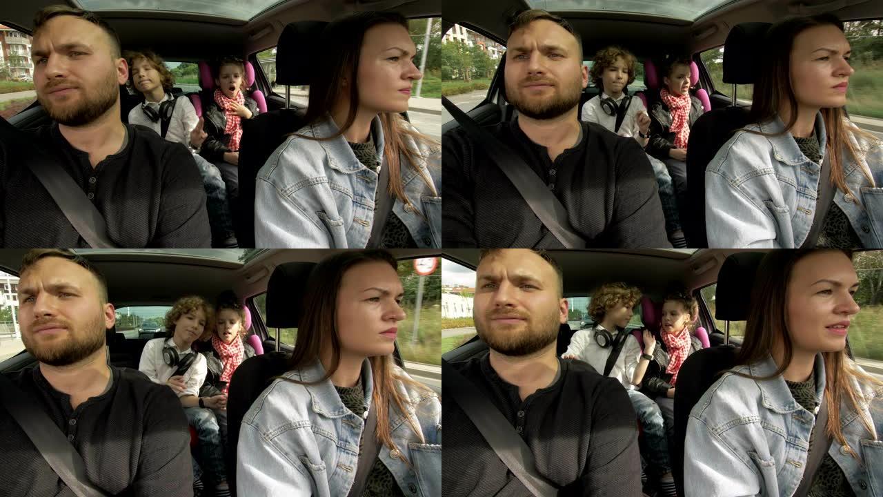从行驶中的车内拍摄: 女人像快乐的男人一样开车，坐在乘客座位上，与坐在后面的小女孩和男孩聊天