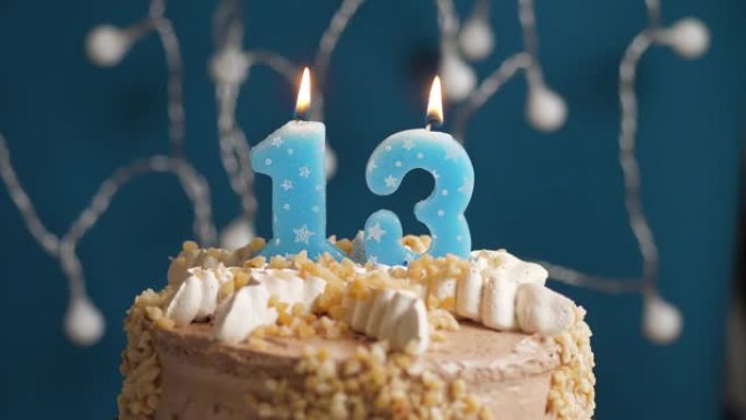 蓝色背景上有13个数字蜡烛的生日蛋糕。蜡烛吹灭了。慢动作和特写视图
