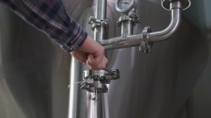 男性酿酒师的特写镜头打开了从啤酒罐到小桶酿造啤酒的水龙头