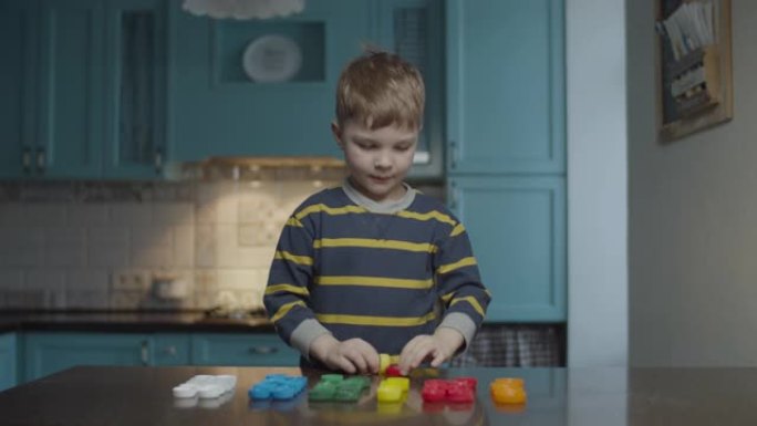 金发学龄前男孩在家庭厨房按颜色分类塑料帽。孩子完成后举起手来。