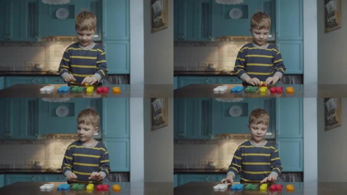 金发学龄前男孩在家庭厨房按颜色分类塑料帽。孩子完成后举起手来。