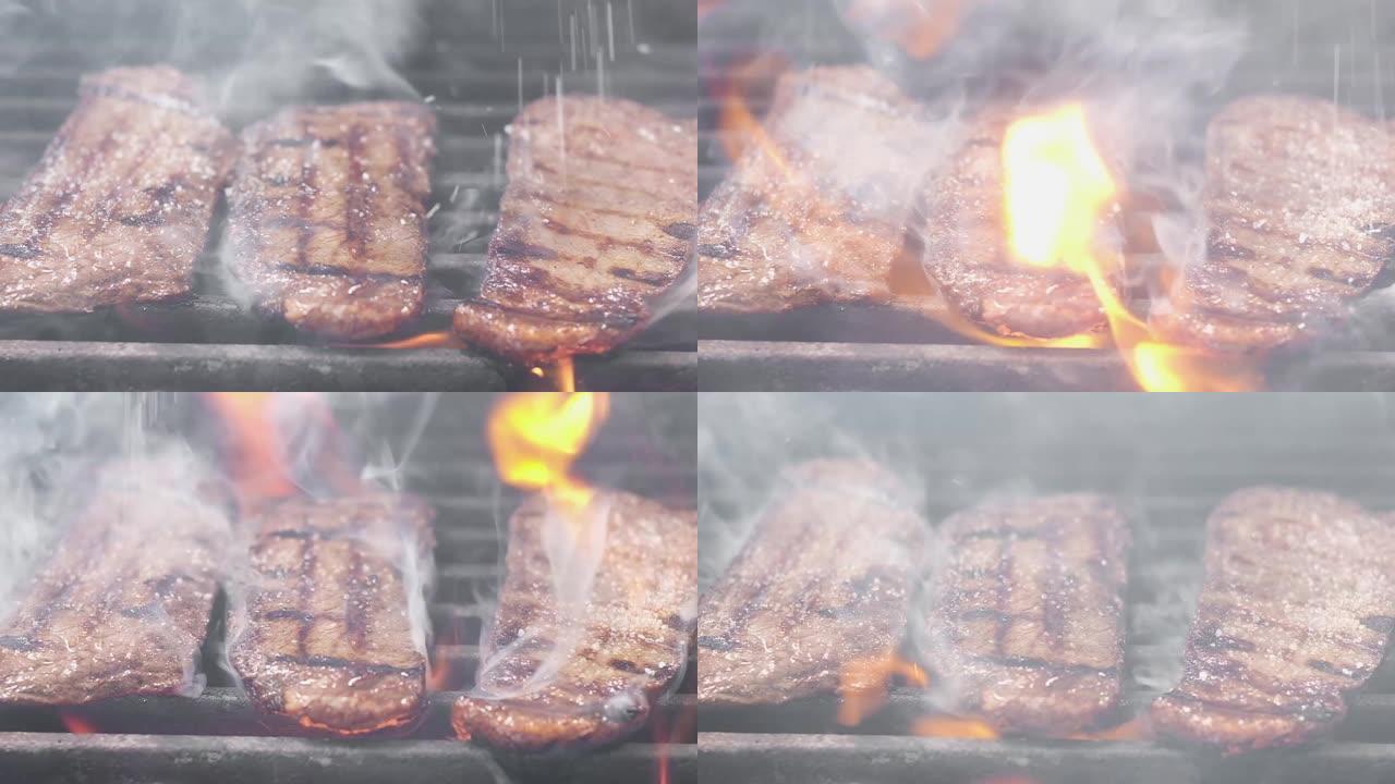 库克在牛排上撒盐。烤架上有三块新鲜的油炸牛排。肉是用火准备的。主厨盐牛肉里脊肉。特写。