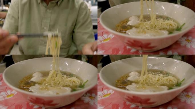 在亚洲，一名游客在用筷子在汤碗里吃面时倾斜