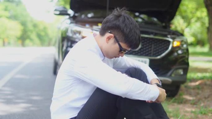 一名年轻的亚洲男子坐在路边一辆破车前