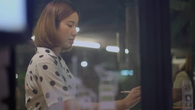 年轻的亚洲妇女晚上在唤醒太空咖啡店的平板电脑上工作到很晚