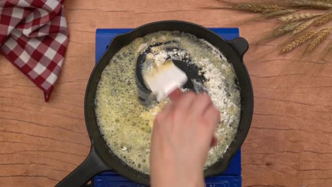 厨师正在将面粉放在锅上，将铁锅的俯视镜头放在煤气炉上，大块黄油在烤架上融化。