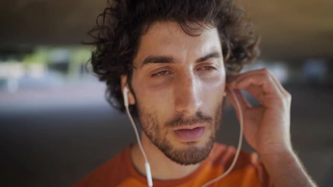 一个健康的年轻人的近距离镜头将耳机放在耳朵里听音乐并深呼吸