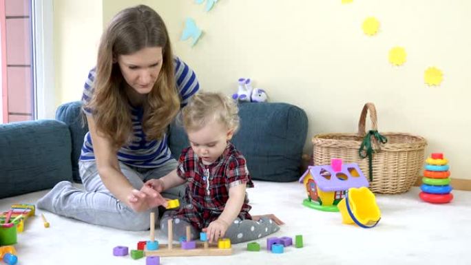 蹒跚学步的女孩和她的母亲在家里玩拉木七彩砖。