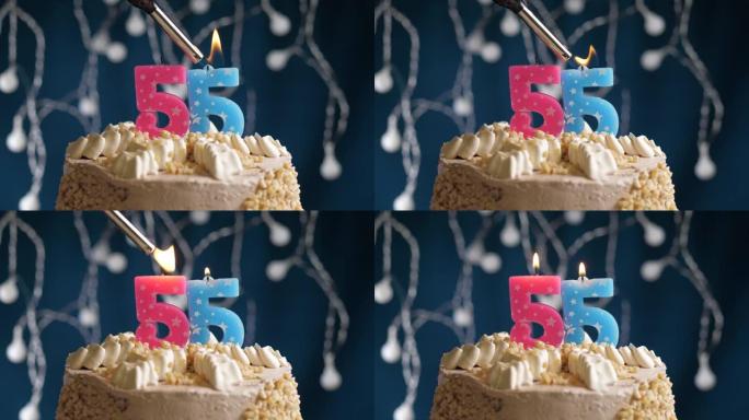 蓝色背景上有55号粉色蜡烛的生日蛋糕。蜡烛着火了。慢动作和特写视图