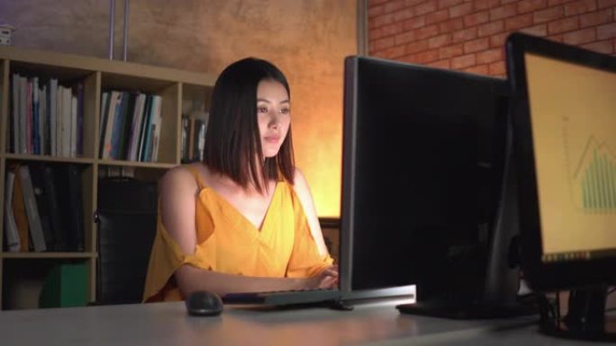 后视图: 亚洲女商人晚上在办公室的计算机上加班 (OT)