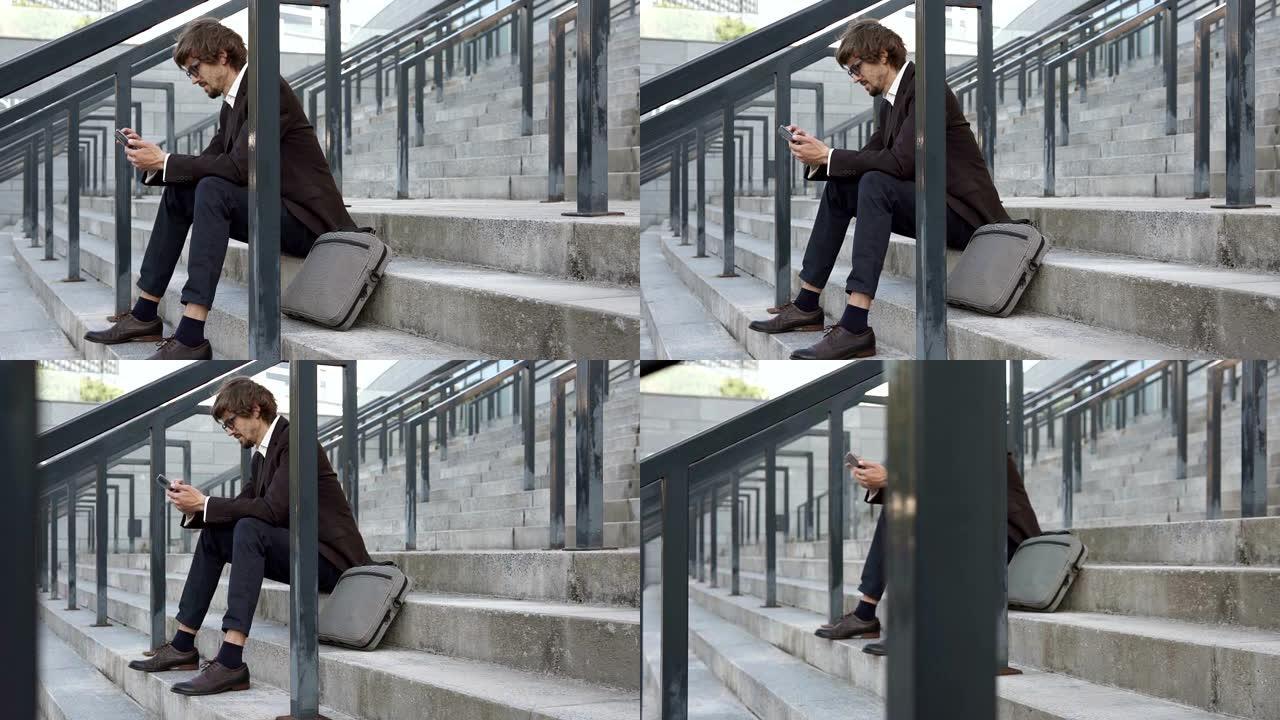一名商人坐在商务中心附近的台阶上，使用智能手机