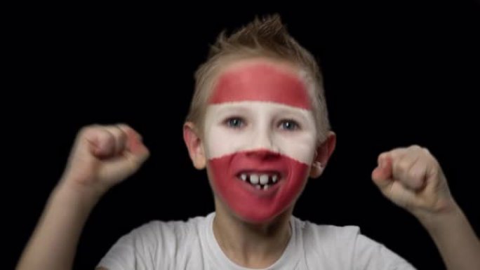 快乐的男孩为他最喜欢的拉脱维亚队的胜利而高兴。脸上涂着民族色彩的孩子。