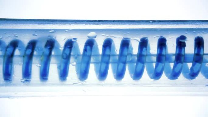 蓝色液体流动，从左到右水平盘旋。科学实验室冷凝器，特写。科学实验室实验中的流体。彩色化学品通过冷凝器