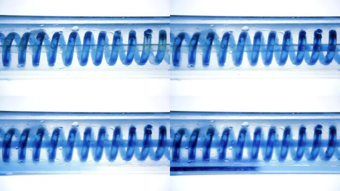 蓝色液体流动，从左到右水平盘旋。科学实验室冷凝器，特写。科学实验室实验中的流体。彩色化学品通过冷凝器