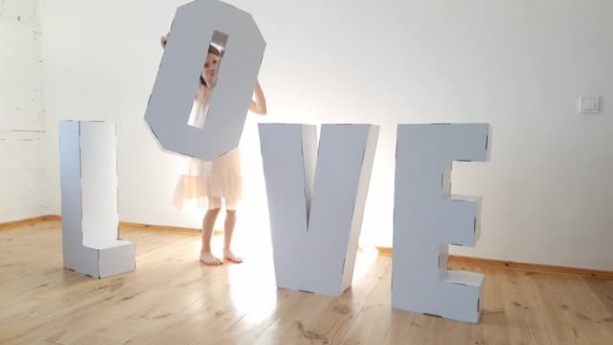 7岁的女孩玩大纸板3D站立字母从白色纸板形成单词爱在一个轻的背景。关系的概念