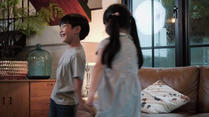 亚洲家庭周年快乐。活跃可爱的小孩儿子和女儿在现代住宅客厅跳着舞。玩得开心的男孩和女孩喜欢在家一起玩有