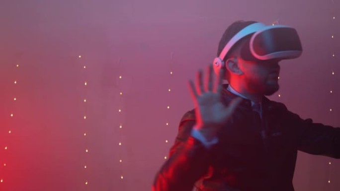 红色照明室内的霓虹灯，戴着虚拟现实眼镜的年轻人，工程师从增强现实中表现出钦佩和惊讶。人迷失在虚拟空间